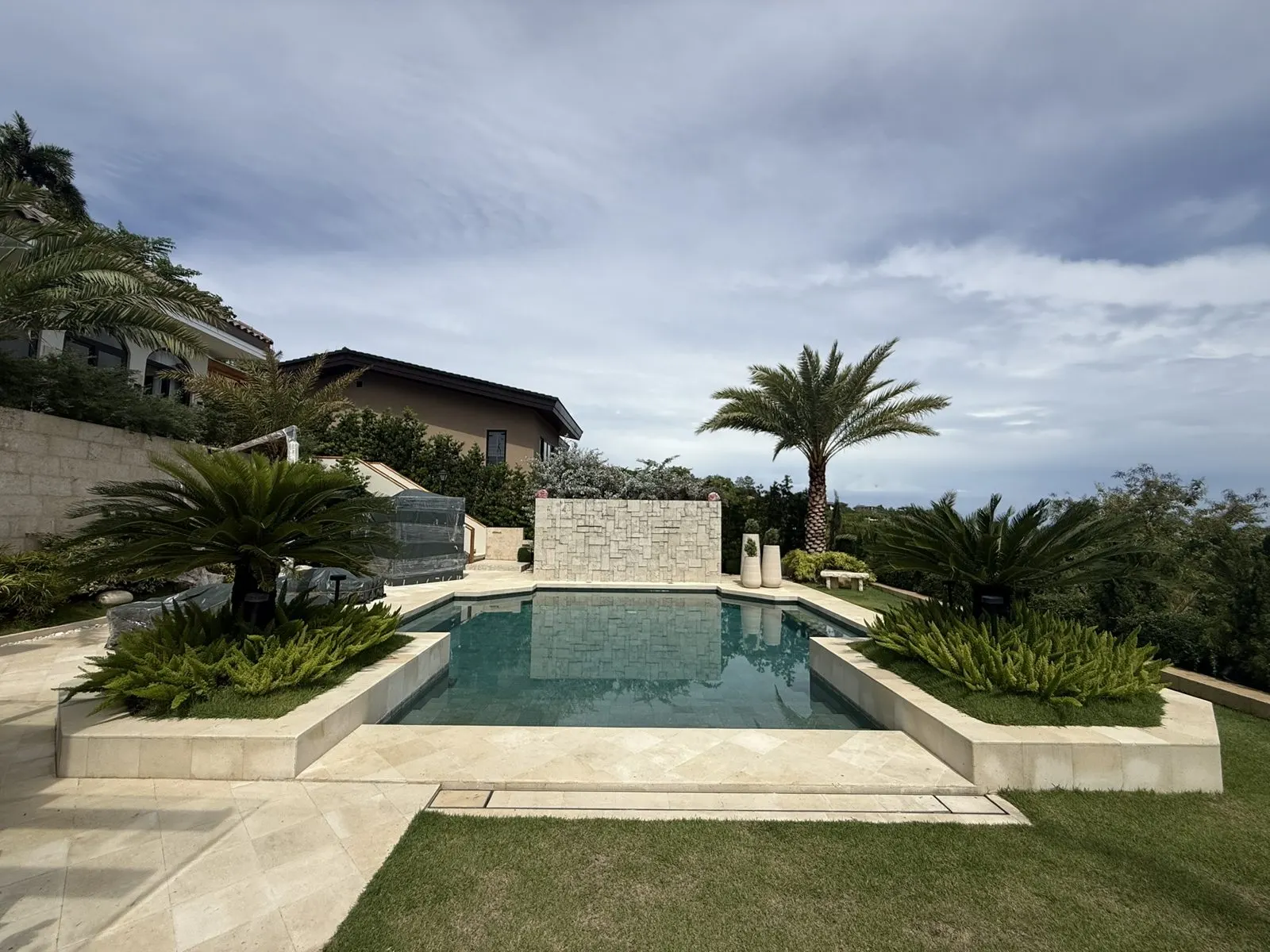 Pool framed by cycads and asparagus ferns with a stone feature wall and sea view