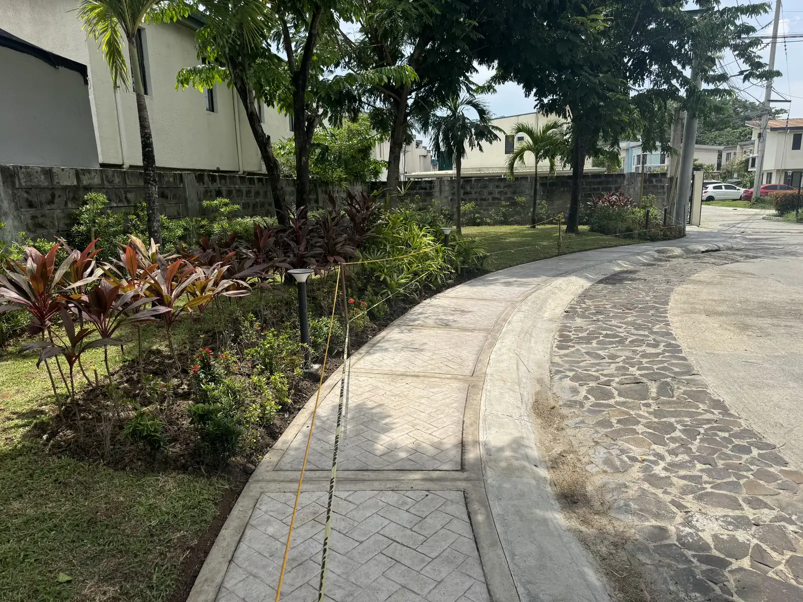 Curved stamped concrete sidewalk beside a stone-paver road and planting bed, Terraces at Tradizo